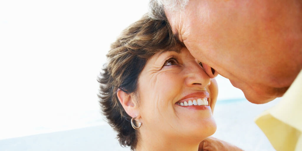 A middle-aged couple is smiling and looking at each other outdoors.