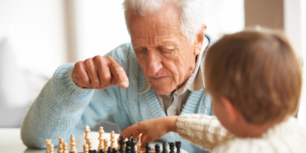 Senior man seated playing chess with a boy