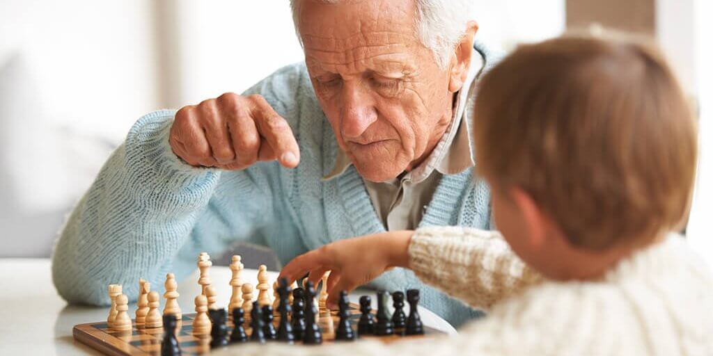 A grandfather teaching his grandson how to play chess